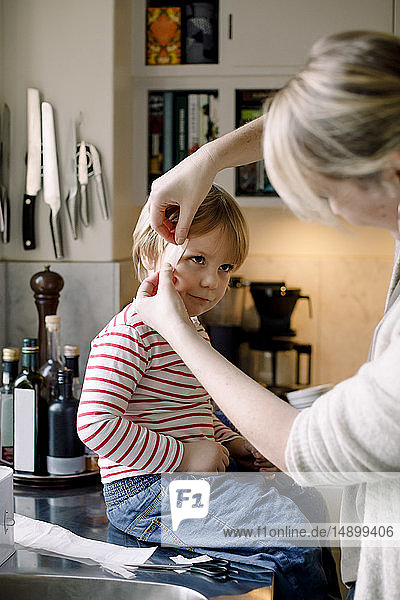 Mutter legt der Tochter zu Hause in der Küche einen Verband auf das Gesicht