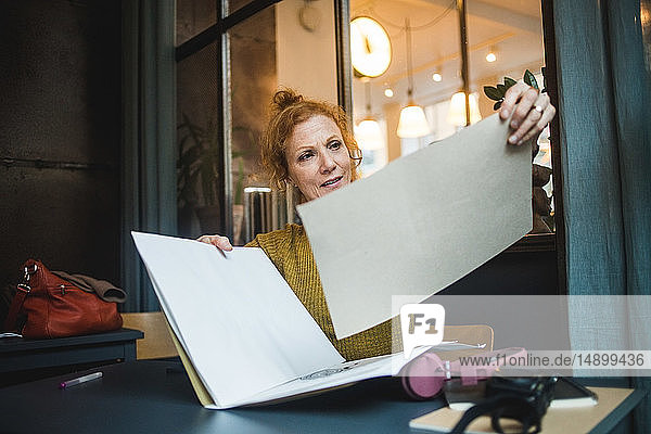 Confident mature female illustrator holding papers at desk in creative office