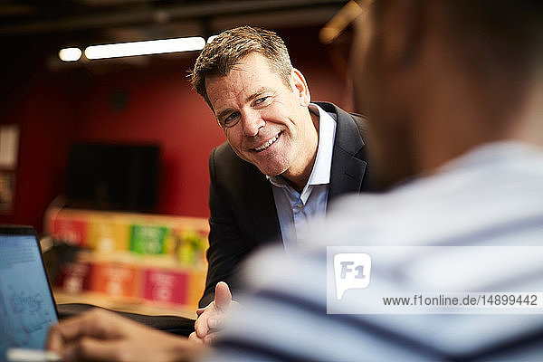 Lächelnder Bankmanager betrachtet männlichen Unternehmer bei einer Präsentation im Kreativbüro