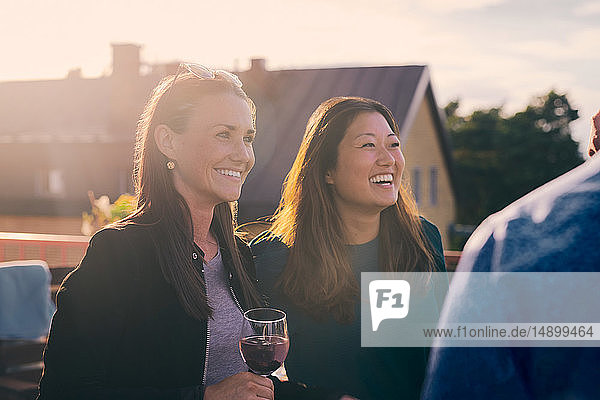 Cheerful friends looking away while standing on terrace during sunset