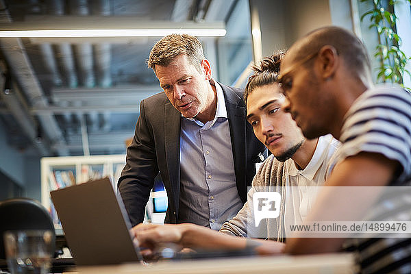 Männliche Unternehmer diskutieren mit Bankmanager über Laptop am Schreibtisch im Kreativbüro