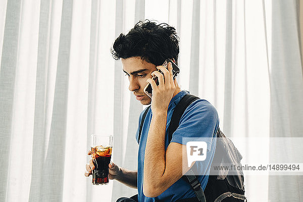 Junger Mann geht im Restaurant mit Cola an ein Smartphone