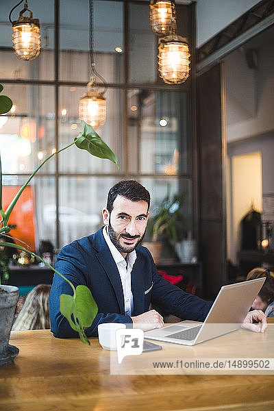 Porträt eines selbstbewussten männlichen Profis  der im Büro am Tisch sitzt