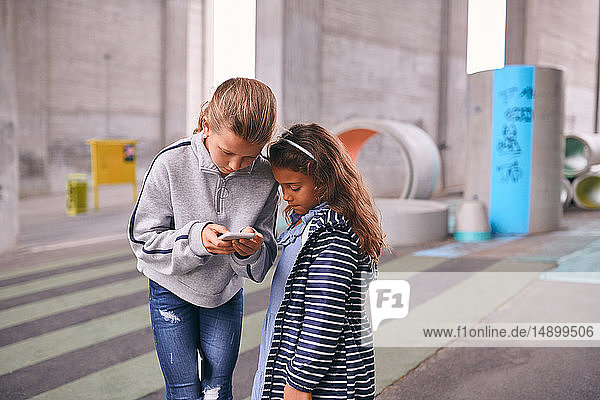 Sisters using mobile phone while standing on footpath at playground