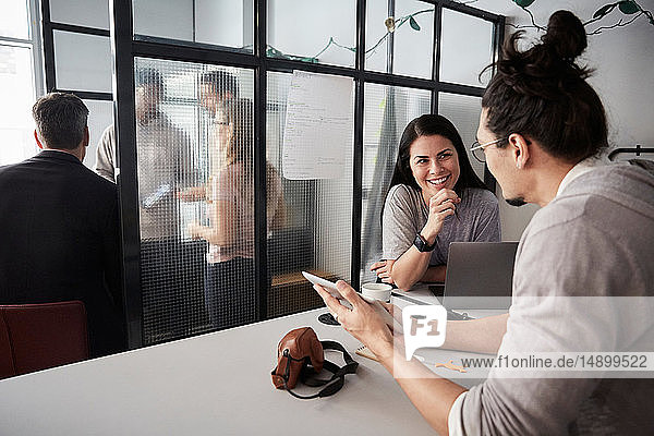 Männlicher Unternehmer diskutiert mit lächelnder Kollegin über digitales Tablet am Schreibtisch im Büro