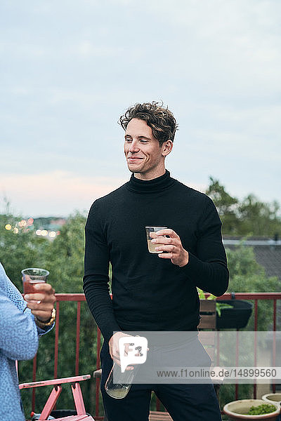 Smiling man holding drink while looking at friend during party