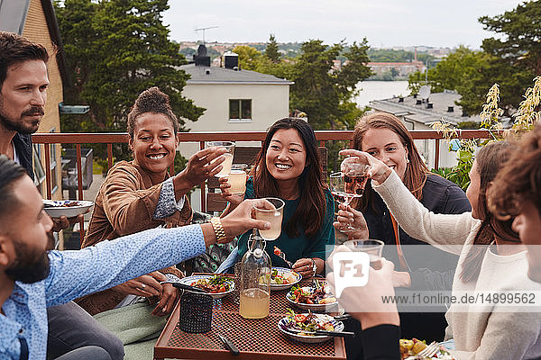 Happy friends toasting drinks while sitting on terrace