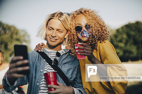 Lächelnder Mann nimmt Selfie mit Freund auf Smartphone mit  während er im Konzert Drinks genießt