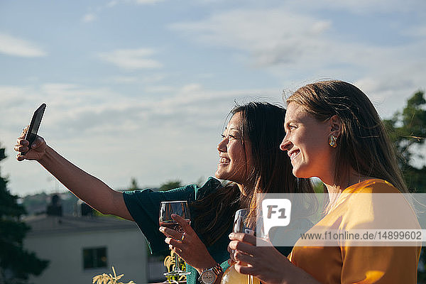 Cheerful female friends taking selfie with mobile phone on terrace during sunny day