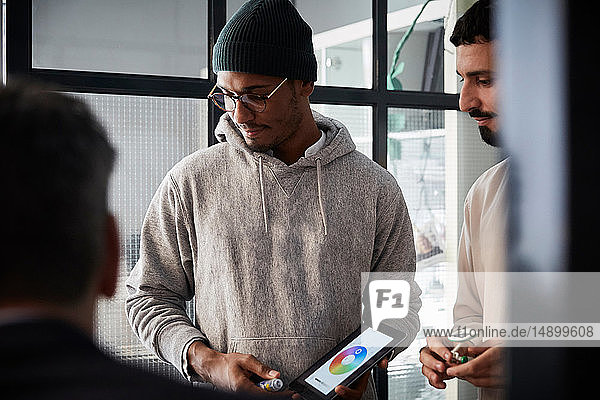 Unternehmer hält digitales Tablet in der Hand  während er während einer Besprechung im Kreativbüro einem Kollegen zur Seite steht