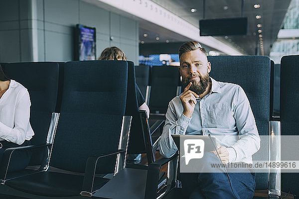 Porträt eines Geschäftsmannes  der mit einem digitalen Tablett im Warteraum im Abflugbereich des Flughafens sitzt