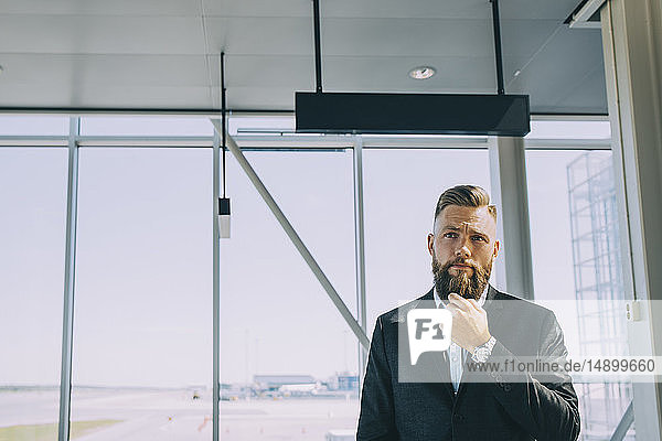 Nachdenklicher Geschäftsmann stellt sich am Flughafen gegen Fenster