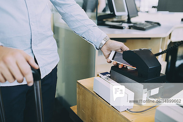 Mittelteil eines Geschäftsmannes scannt Ticket auf Smartphone am Flughafen-Check-in-Schalter