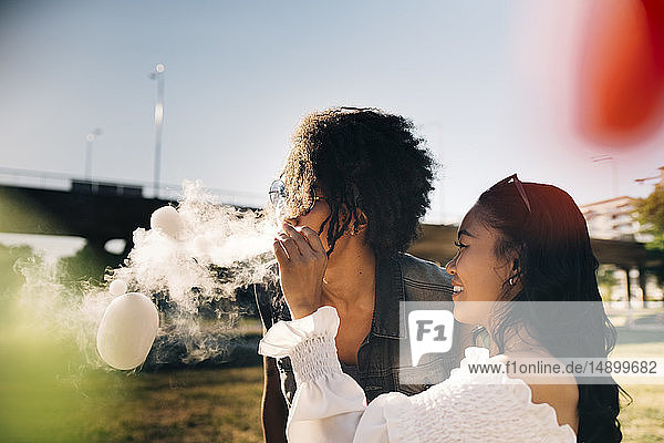 Playful woman looking at man exhaling smoke bubbles in music festival