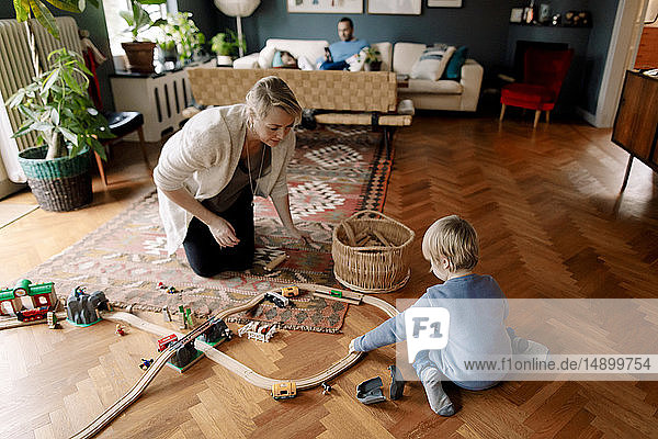 Mutter betrachtet Tochter beim Spielen mit der Eisenbahn im Wohnzimmer