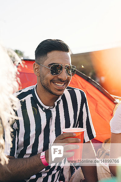 Smiling young man wearing sunglasses having drink during music festival on sunny day