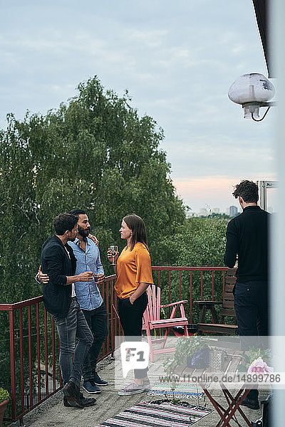 Freunde unterhalten sich in voller Länge  während sie während des geselligen Beisammenseins auf der Terrasse stehen