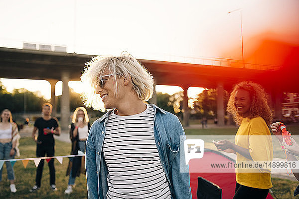 Lächelnder junger Mann genießt mit Freunden bei einer Musikveranstaltung an einem sonnigen Tag