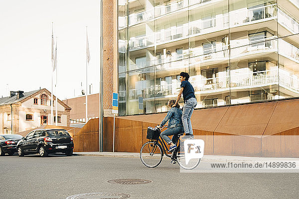 Seitenansicht eines jungen Mannes auf dem Fahrrad mit einem Freund auf der Straße in der Stadt