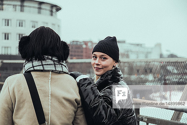 Porträt einer selbstbewusst lächelnden Frau in warmer Kleidung  die im Winter mit einem Freund in der Stadt steht