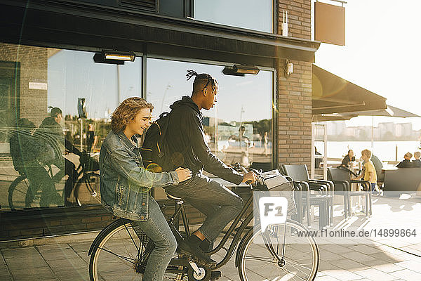 Jugendlicher Junge fährt mit fröhlichem Freund bei Sonnenschein Fahrrad in der Stadt
