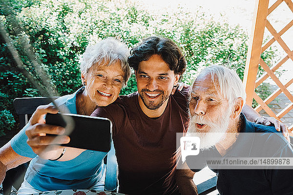 Lächelnder männlicher Hausmeister beim Selfie mit älterem Mann und Frau im Hinterhof