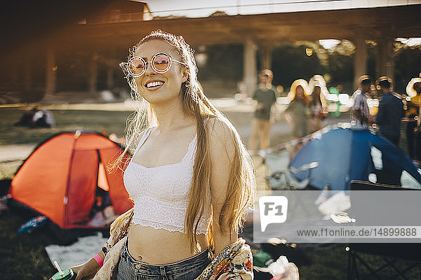 Porträt einer lächelnden jungen Frau mit Sonnenbrille beim Musikfestival stehend