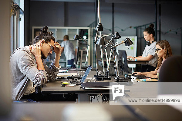 Angespannter männlicher Unternehmer schaut auf Laptop  während er im Kreativbüro sitzt