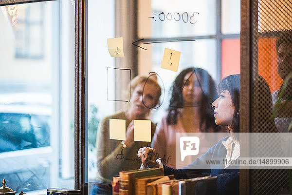 Geschäftsfrau plant Strategie auf Glaswand mit Kollegen aus dem Kreativbüro