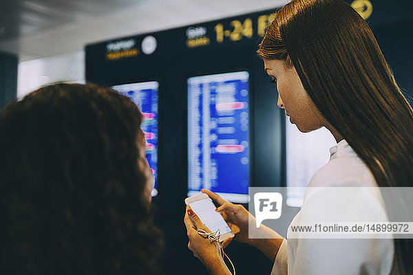 Junge Geschäftsfrau überprüft Flugzeiten über Smartphone am Flughafen