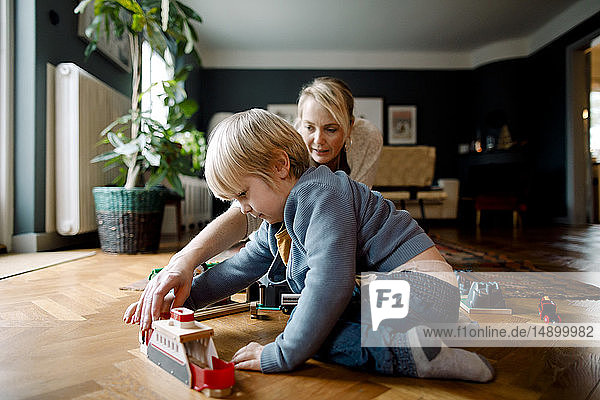 Mutter und Tochter spielen zu Hause mit der Spielzeugeisenbahn auf dem Hartholzboden im Wohnzimmer