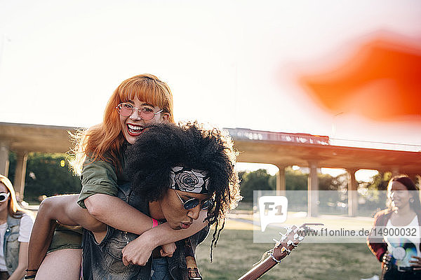 Young man piggybacking happy friend while enjoying in music festival
