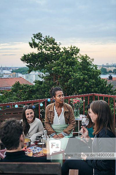 Fröhliche Freunde genießen das gesellige Beisammensein auf der Terrasse bei Sonnenuntergang