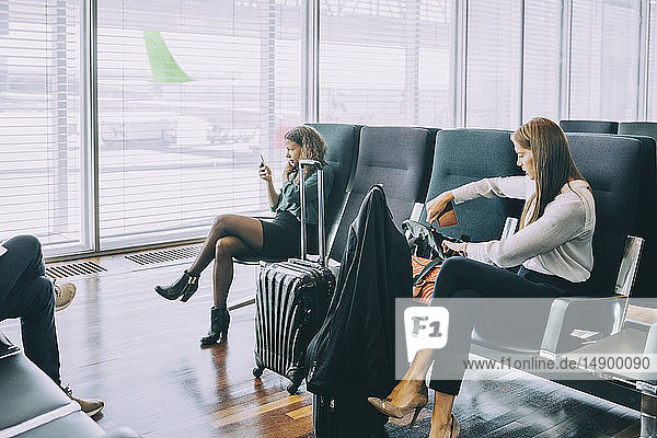 Junge Geschäftsfrau nimmt Pass aus der Handtasche  während sie im Abflugbereich des Flughafens sitzt
