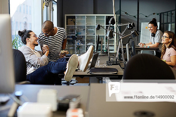 Männliche Unternehmer lächeln  während sie sich am Schreibtisch im Kreativbüro begrüßen