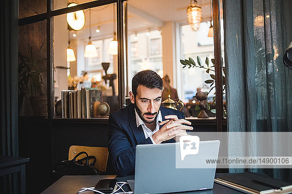 Confident businessman with hands clasped looking at laptop on desk in creative office