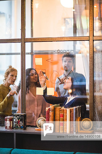 Zuversichtliche Geschäftsfrau plant Strategie auf Glaswand mit Kollegen im Kreativbüro