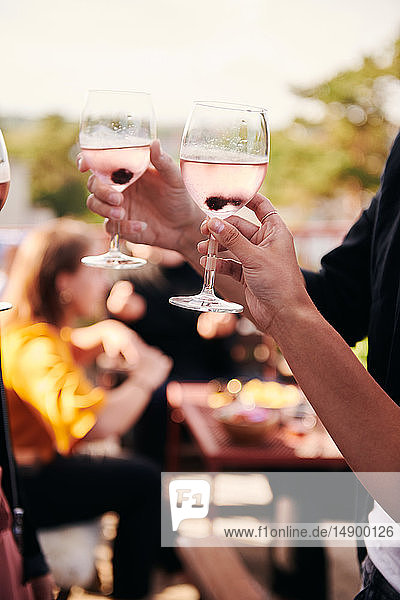Geschnittene Hände von Freunden mit Weingläsern während eines geselligen Beisammenseins auf der Terrasse