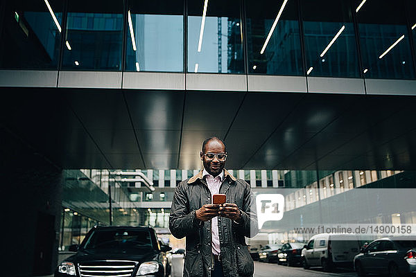 Schwacher Blickwinkel auf einen Geschäftsmann  der ein Smartphone benutzt  während er auf der Straße vor einem Gebäude in der Stadt steht