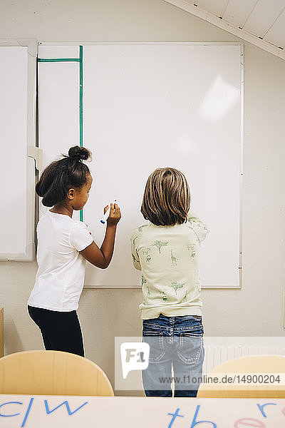 Rückansicht eines Jungen und eines Mädchens  die in der Grundschule auf einer Tafel schreiben