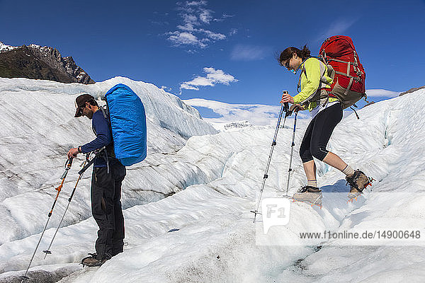 Couple backpacking across the Root Glacier with crampons on during summer  Donoho Peak peaking out in the background  Wrangell Mountains  Wrangell-St. Elias National Park  South-central Alaska; Kennicott  Alaska  United States of America