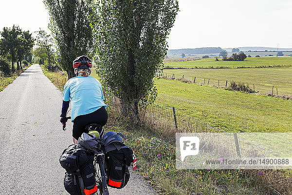 Radfahrerin auf einem bewaldeten Radweg mit Feldern in der Ferne  nördlich von Bastogne; Belgien