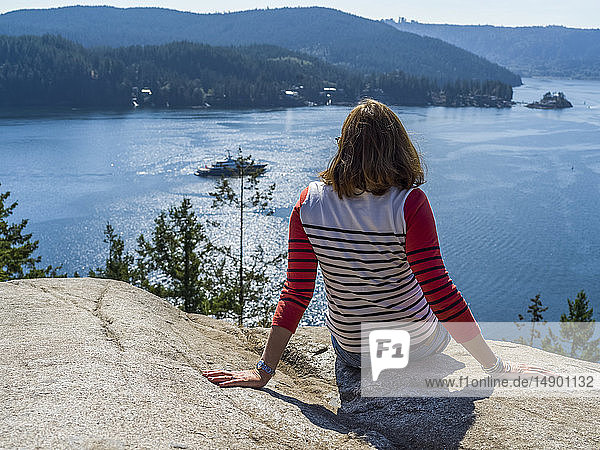 Eine Frau sitzt am Quarry Rock auf dem Baden-Powell Trail und blickt auf die Küste  Deep Cove  North Vancouver; Vancouver  British Columbia  Kanada