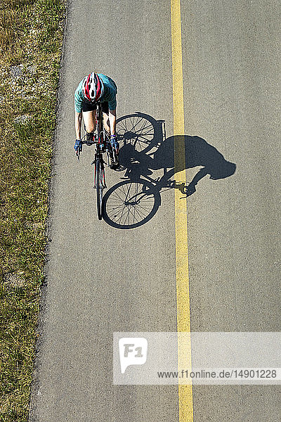 Luftaufnahme mit Blick auf eine Radfahrerin auf einem gepflasterten Weg mit Schatten der Radfahrerin; Calgary  Alberta  Kanada