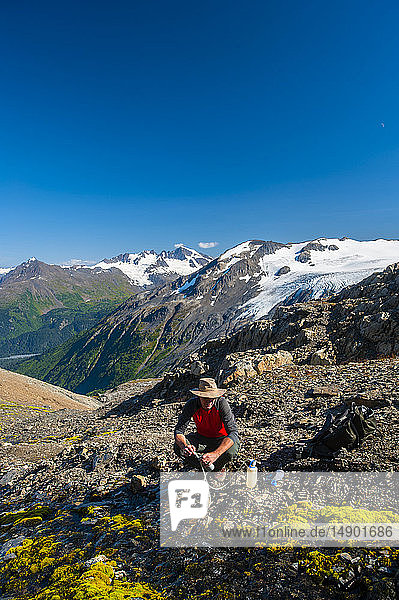 A man is seen filtering water while hiking the beautiful Harding Icefield Trail in Kenai Fjords National Park with a hanging glacier in the background; Alaska  United States of America
