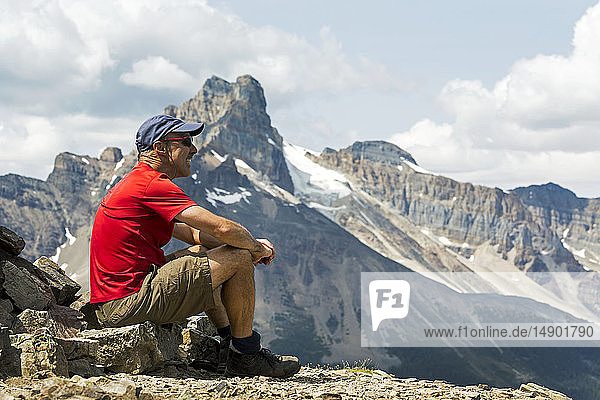 Männlicher Wanderer auf einem Felsen sitzend mit Blick auf eine Berglandschaft im Hintergrund; British Columbia  Kanada