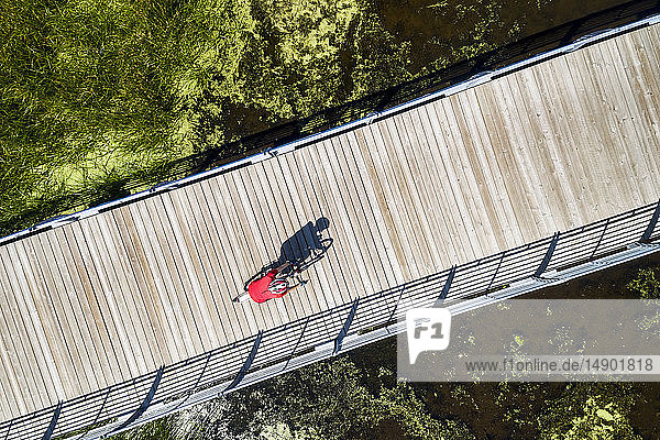 Aerial view looking straight down on a female cyclist on a bridge across a swampy pond with shadow of cyclist  East of Calgary; Alberta  Canada