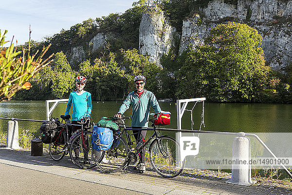 Weiblicher und männlicher Radfahrer stehen auf einem Radweg entlang eines Geländers am Flussufer mit Klippen im Hintergrund und blauem Himmel  südlich von Namur; Belgien