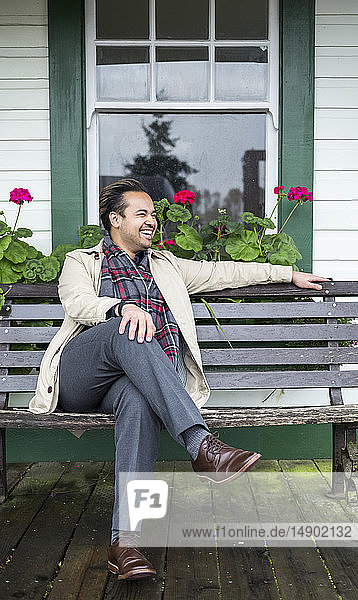 A man sits on a bench outside a building and laughs as he looks away; Fort Langley  British Columbia  Canada