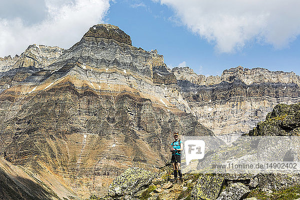Female hiker on rocky pathway with mountain  blue sky and clouds in the background; British Columbia  Canada